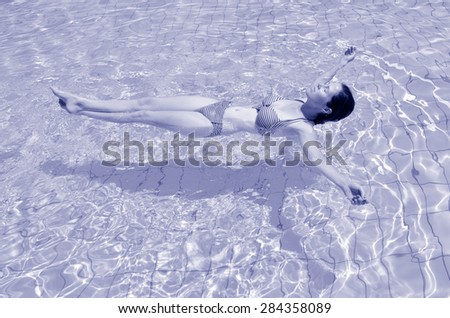 Young woman floating on natural mineral salty water in outdoor pool in resort at the Dead Sea, Israel