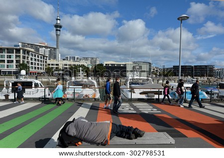 AUCKLAND - AUG 01 2015:Homeless sleep on a bench in Viaduct Harbour against Auckland skyline.In 2104 Statistics New Zealand estimated about one in 120 New Zealanders were homeless or housing deprived.