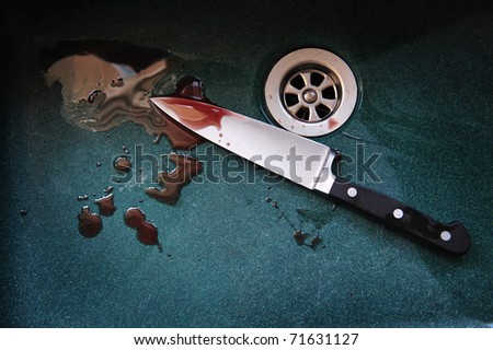 A knife with drops of blood on it resting in a dark green sink. Concept photo of murder and crime