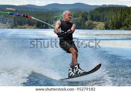 A water skier in his 60's preforming water skiing sport on a lake.