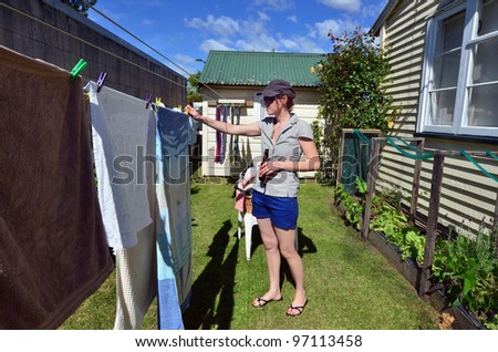 A young smiling woman drinks beer while hanging clothes on clothes line using clothes peg.