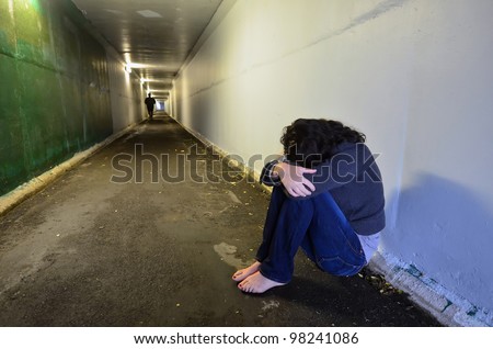 Crime scene concept photo of rape victim. A sad woman sits on the floor of a dark tunnel.