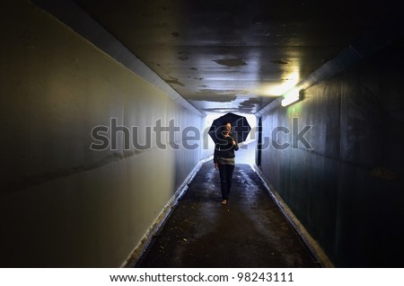 A young woman holds an umbrella and walks through a tunnel. Light at End of Tunnel concept.