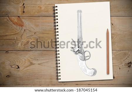 Drawing of old Europe gun on notebook or sketchbook  and pencil lay over. On old wooden table.
