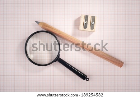magnifying glass, pencil and sharpener over graph paper, selective focus