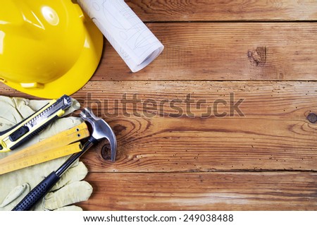 hammer, protective gloves, folding ruler, model knife, blueprint and yellow safety helmet on wooden background