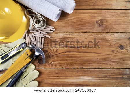 hammer, protective gloves, folding ruler, model knife, blueprint,  wooden dowels, electrical cable  and yellow safety helmet on wooden background