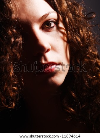 A low-key portrait about an attractive lady with white skin and long brown wavy hair whose look is glamorous