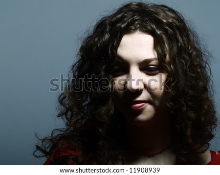 A low-key portrait about a pretty lady with white skin and long brown wavy hair who is looking down and titters