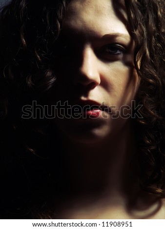 A dark low-key portrait about a pretty lady with white skin and long brown wavy hair whose look is attractive