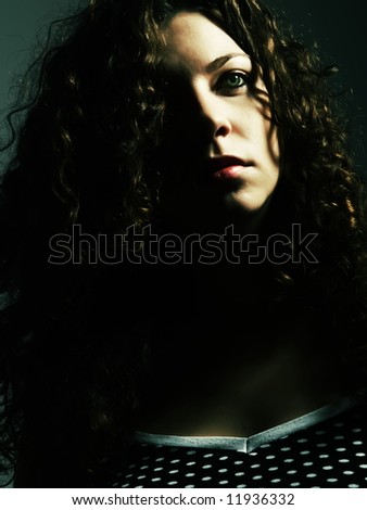 A low-key portrait about a pretty lady with white skin and long brown wavy hair whose look is enchanting and she wears a nice black dress with white dots