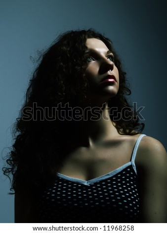 A low-key portrait about a pretty lady with white skin and long brown wavy hair who wears a nice black dress with white dots and she is looking up and she wishes something