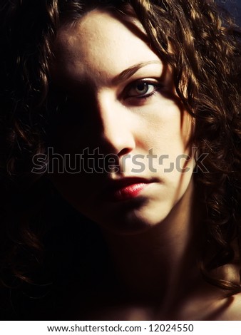A low-key portrait about a pretty lady with white skin and long brown wavy hair whose look is attractive