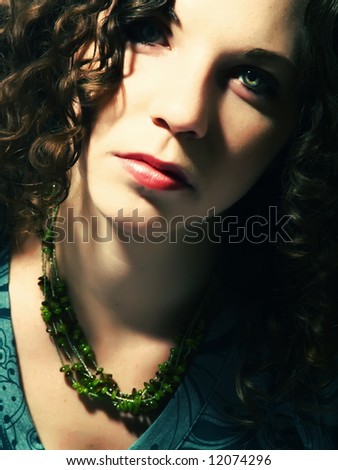 A portrait about a pretty lady with white skin, long brown wavy hair whose look is glamorous and she wears a nice green dress and necklace