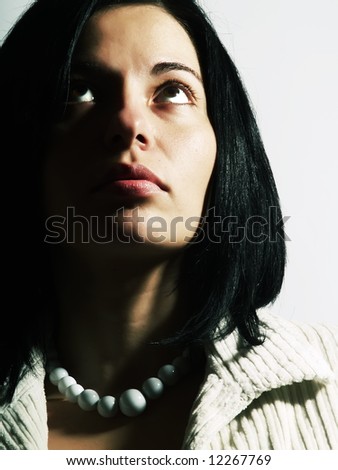 A high-key portrait about a happy attractive lady with black hair who is looking up and she is dreaming. She is wearing a white coat and a white necklace.