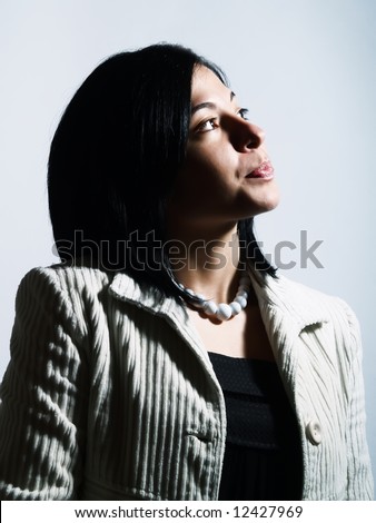 A high-key portrait about a young pretty woman with black hair who is looking up and she is dreaming. She is wearing a white coat, a black dress and a white necklace.