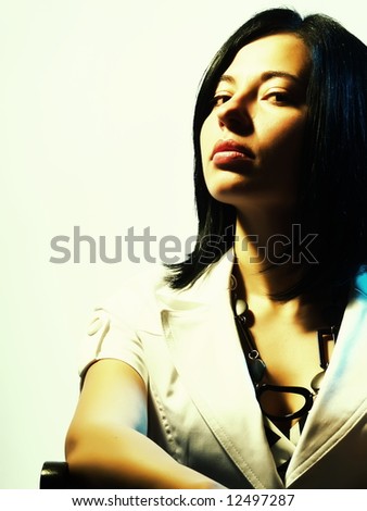 A high-key portrait about a pretty trendy woman with black hair who is lighted in blue and yellow, she is sitting on a chair, she is looking up and she is dreaming something.