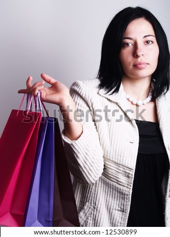 A high-key portrait about a pretty trendy lady with black hair who is holding some shopping bags and she has an attractive look. She is wearing a white coat, a black dress and a white necklace.