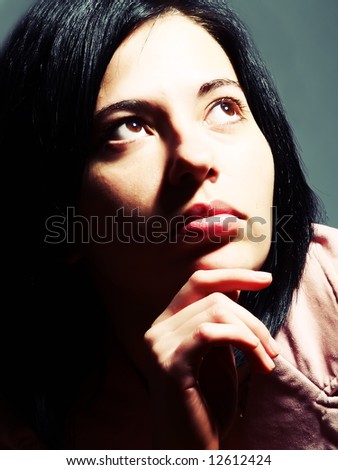 A closeup high-key portrait about an elegant trendy woman with black hair who is looking up and she is admiring something. She is wearing a stylish pink coat.