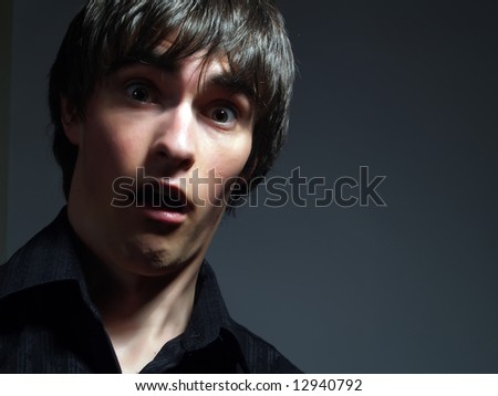 A portrait about a trendy handsome young man who is looking towards and he is surprised or scared. He is wearing a stylish black shirt.