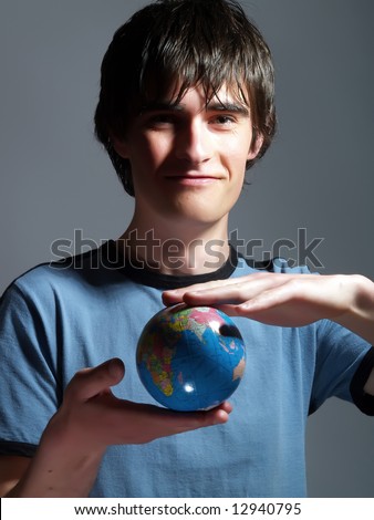 A portrait about a trendy attractive young man who is smiling, he is holding a globe in his hands and he is planning his holiday. He is wearing a blue t-shirt.