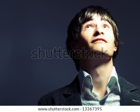 A portrait about a trendy handsome guy who is looking up and he is dreaming something. He is wearing a white shirt and a black suit.