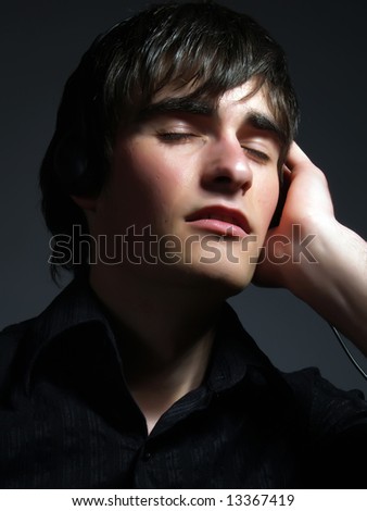 A portrait about a trendy handsome young guy who is smiling, he is listening to music and he is relaxing. He is wearing a stylish black shirt.