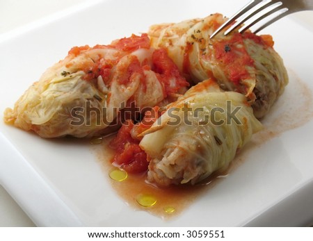 Fork pierces stuffed cabbage roll on white plate.