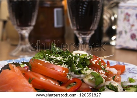 Greens and sesame seeds in a vegetable salad with tomatoes, cucumbers and onions on a background of glasses of red wine