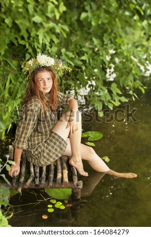 A girl in a wreath sitting on the bank of a river