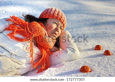 A european woman lying on the snow with tangerines around her