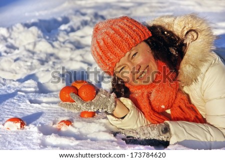 A european woman lying on the snow with tangerines in her hands