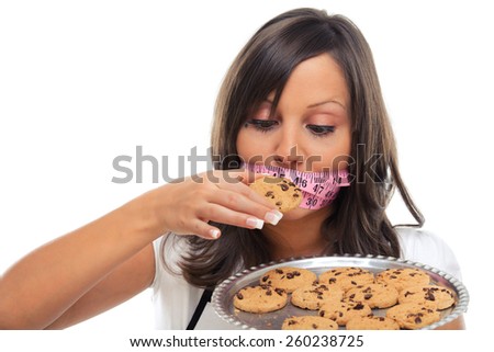 Young woman holding a tray with homemade chocolate cookies and tied mouth with measuring tape, looking at them