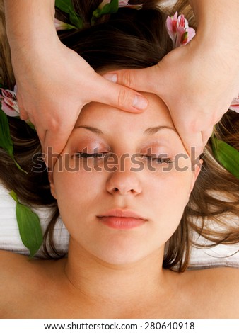 Young woman lying on white background with flowers in her hair waiting in spa studio for massage