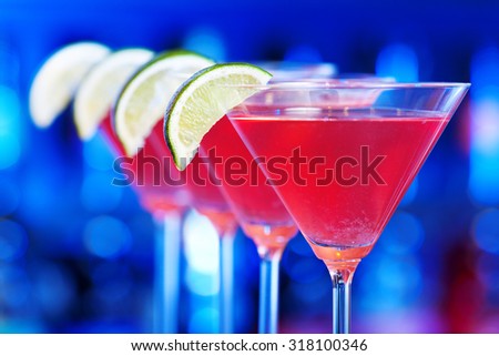Row of four Cosmopolitan cocktails on a bar counter in a club shot in dim blue light