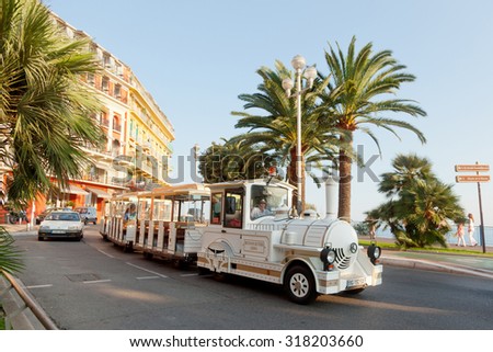 Nice, France - July 01, 2011 : Nice street live at sunset - white fun trackless train for sightseeing in front, one car at the background and pedestrians walking on Promende des Anglais