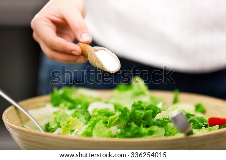 Young woman making salad in the kitchen. Pouring salt.