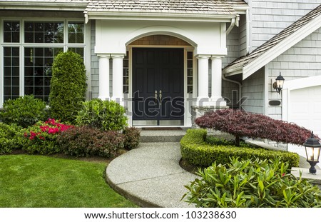 Front Door to home surrounded by seasonal plants and part yard and sidewalk in forefront