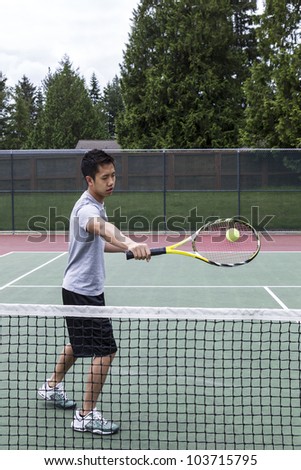 Young Asian Man using backhand volley on outdoor tennis court