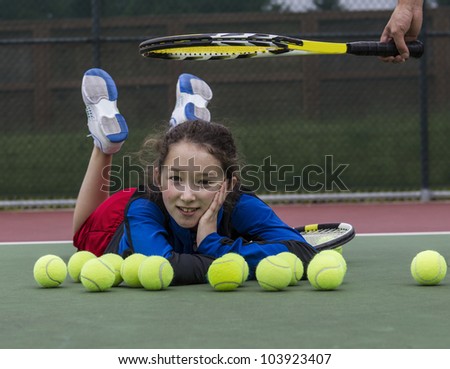 Young girl having fun on outdoor tennis courts with coach\'s racket above her head