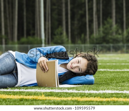 Young girl studying on soccer field with woods in background