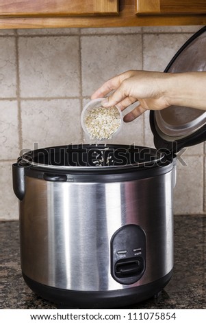 Hand pouring brown and white rice into rice cooker on stone counter top in kitchen