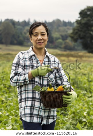 Mature women standing in bean field with basket of vegetables with trees and sky in background