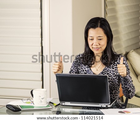 Mature women giving thumbs up on data results while working at home office