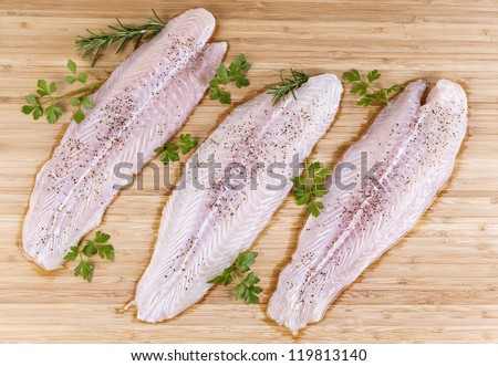Three fresh white fish fillets with seasoning and herbs on bamboo board