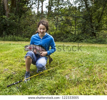 Young girl with eyes closed giving thanks after landing a large trout with woods in background