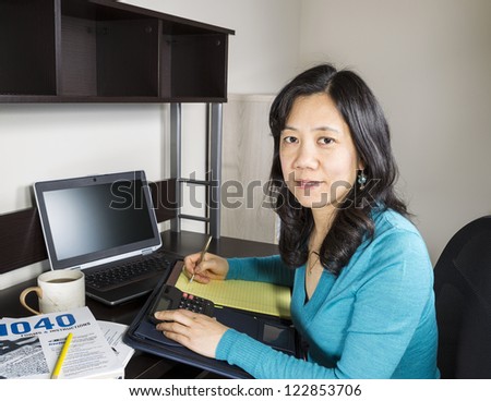 Mature Asian women doing year end taxes with tax form booklet and computer on desk