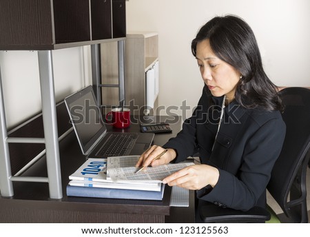 Professional Mature Asian woman  doing income taxes with tax form booklet, calculator, coffee cup and computer on desk