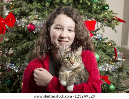 Young girl holding gray hair tabby cat with Christmas tree in background