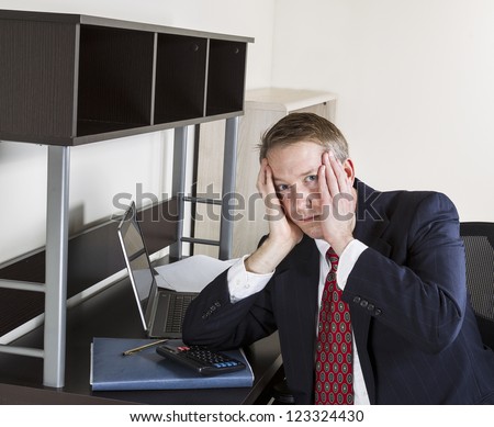 Mature man stressed out at work with computer, calculator, pen and papers on desk
